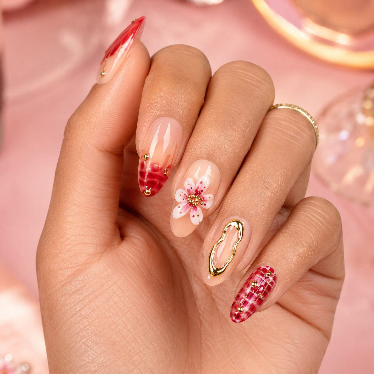Medium tan skin hand wearing red floral gold press-on nails with glossy nude base and plaid accent nail