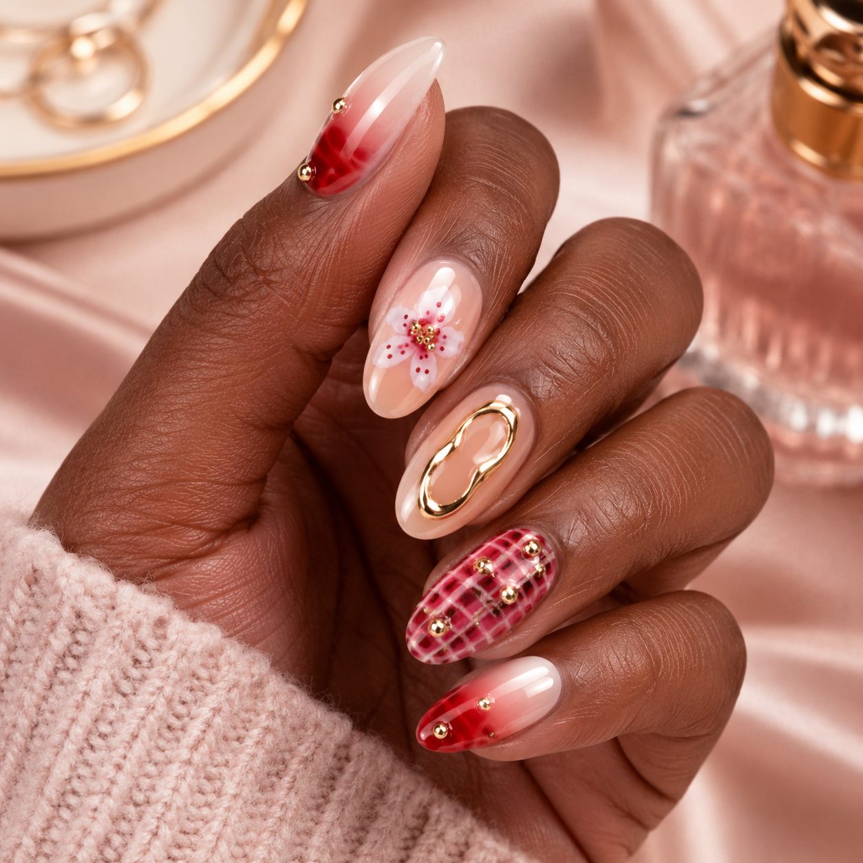 Deep skin tone hand wearing elegant red nude press-on nails with floral details, gold accents, and glossy finish