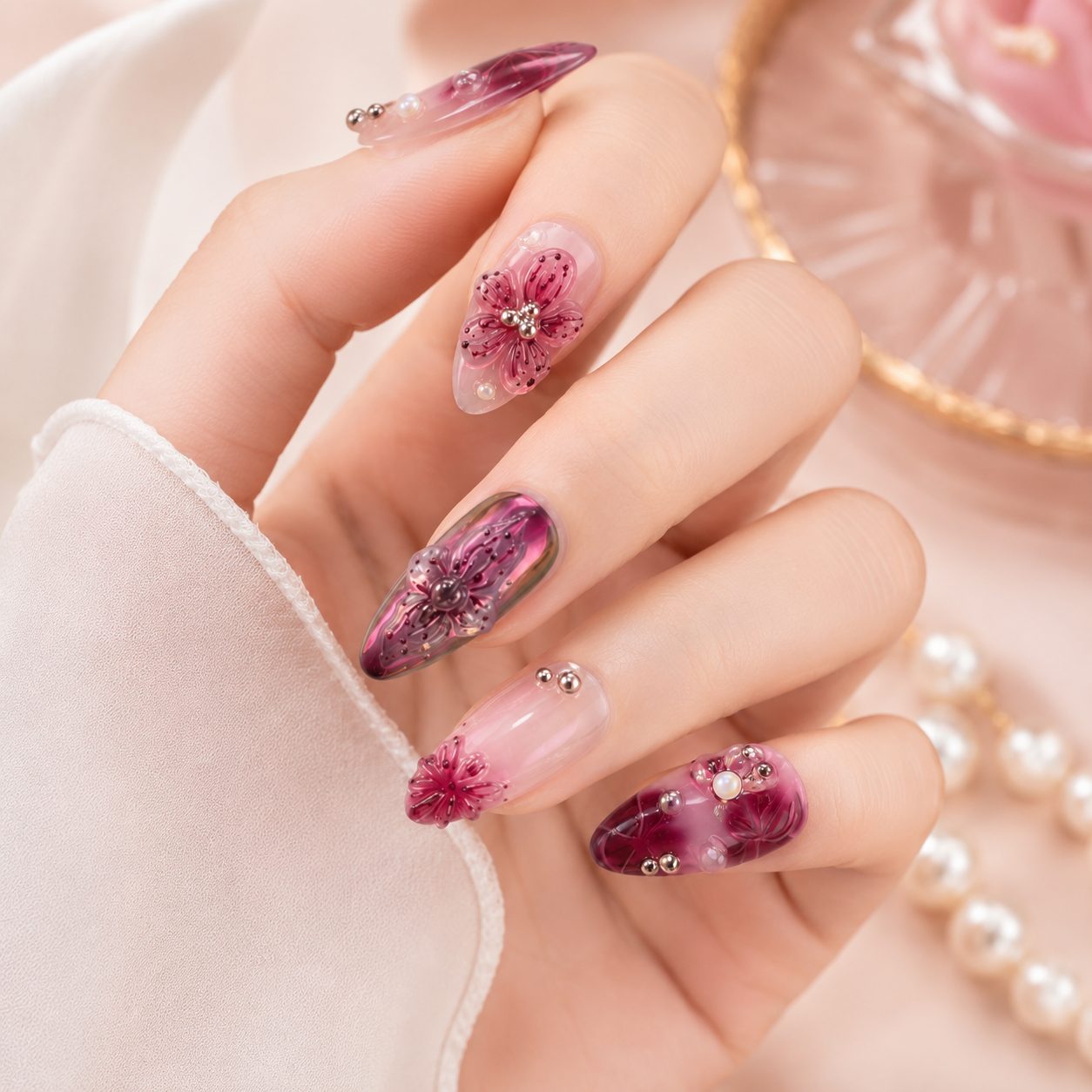 Light skin hand wearing glossy burgundy pink 3D floral press on nails with pearl and rhinestone details.