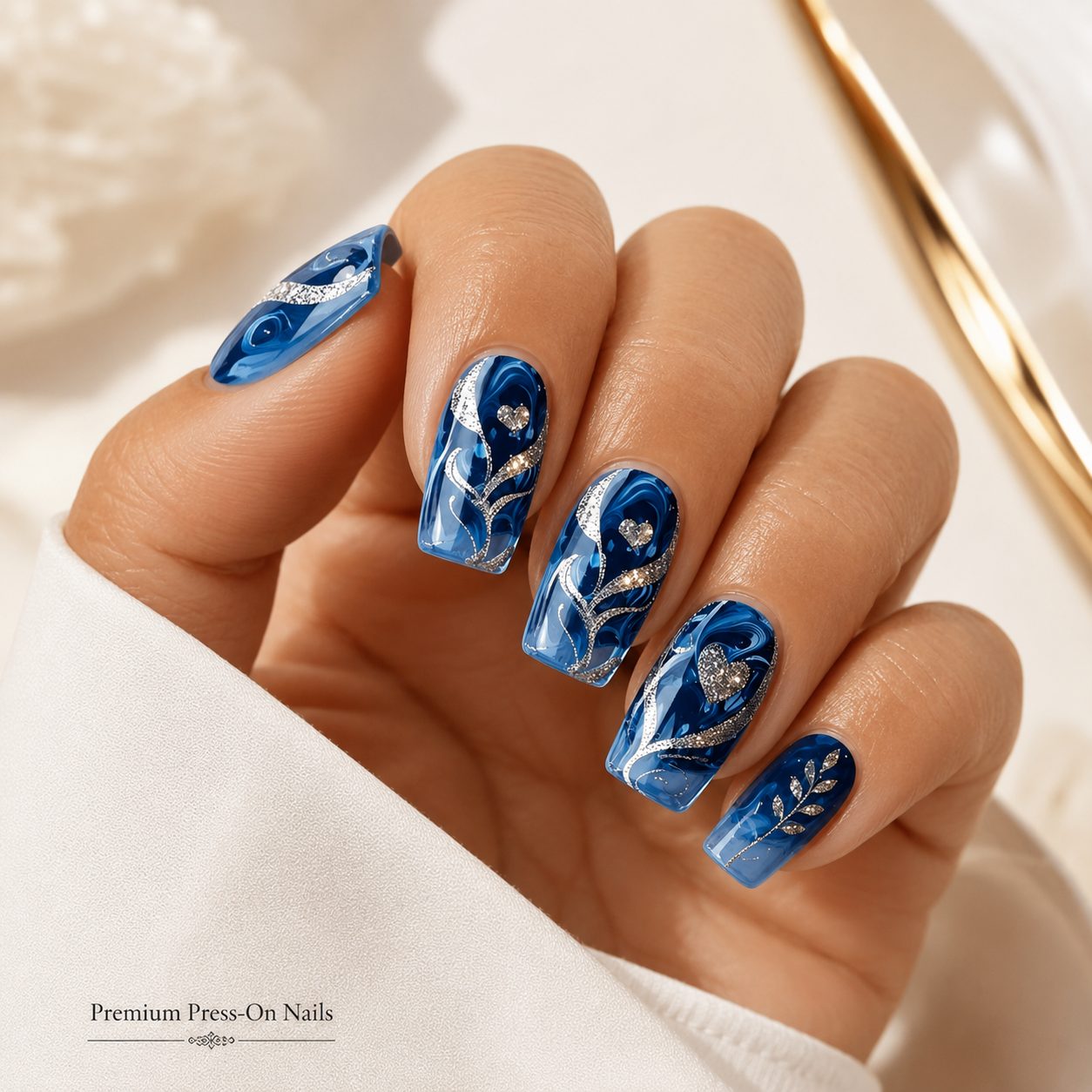 Tan skin hand wearing ocean blue marble press-on nails with silver glitter swirls, glossy finish, and premium reusable nail design.