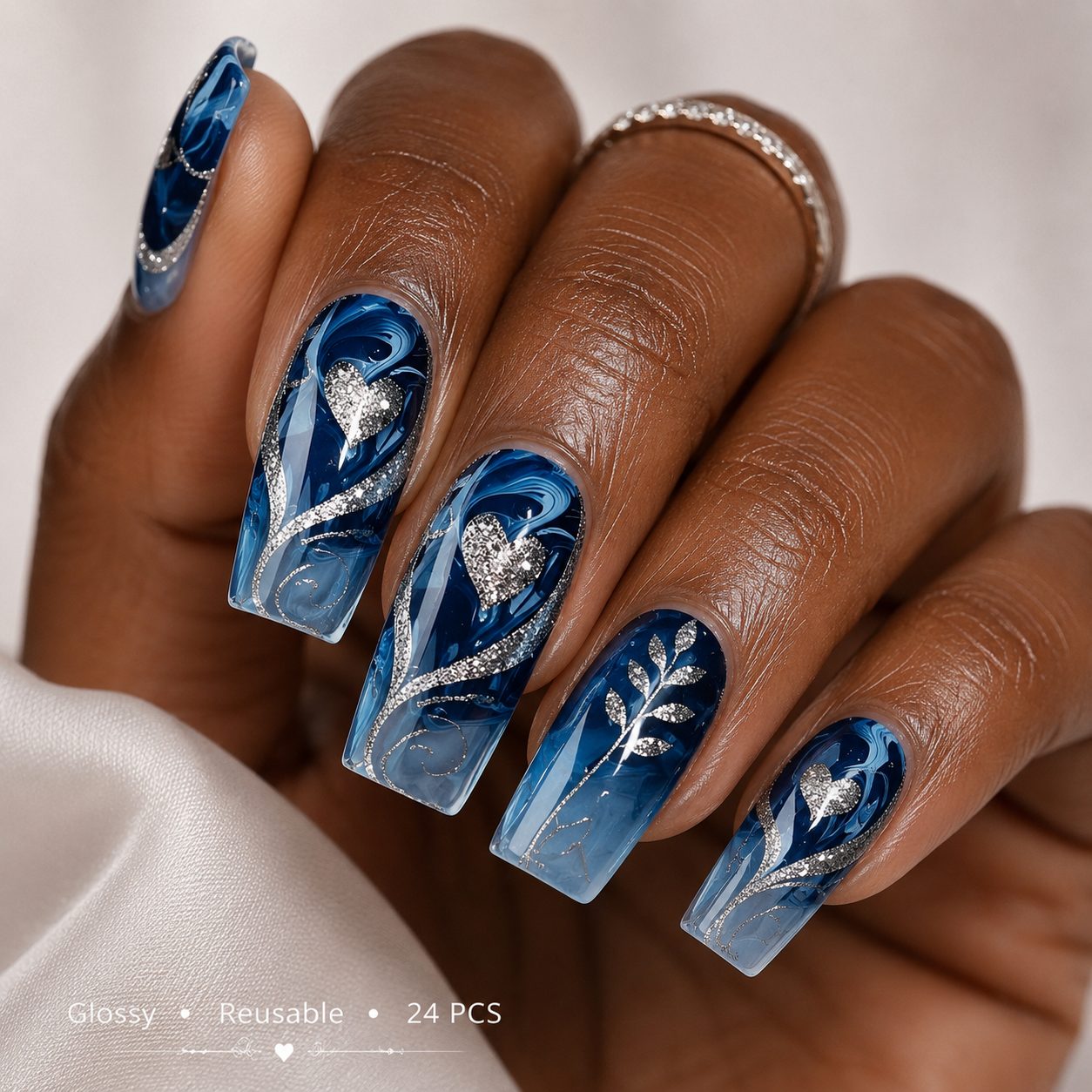Deep brown skin hand wearing luxury blue marble press-on nails with silver glitter heart accents, glossy reusable 24 pcs false nails.